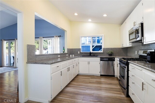 kitchen with stainless steel appliances, white cabinetry, vaulted ceiling, and light hardwood / wood-style flooring