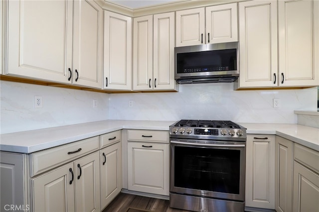 kitchen with stainless steel appliances, cream cabinets, backsplash, and dark wood-type flooring