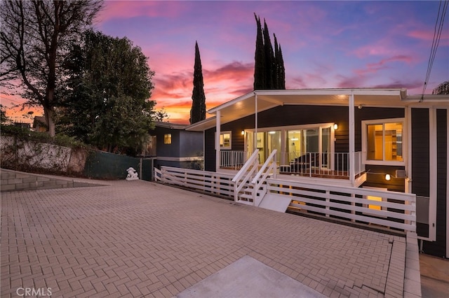 back house at dusk featuring covered porch