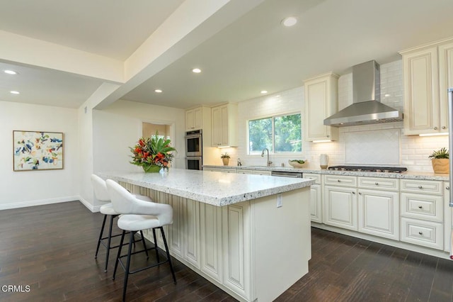 kitchen featuring light stone counters, wall chimney exhaust hood, gas stovetop, dark hardwood / wood-style floors, and a breakfast bar