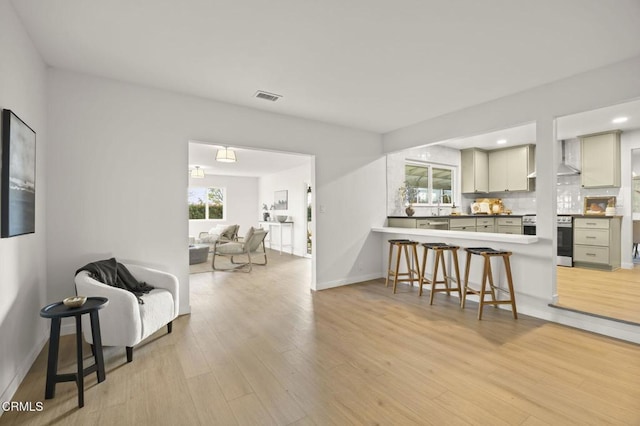 kitchen featuring light wood-type flooring, stainless steel range, kitchen peninsula, a breakfast bar, and backsplash