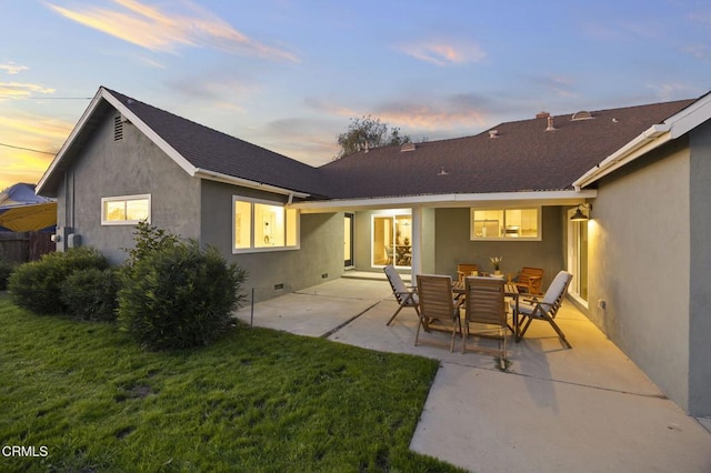 back house at dusk featuring a lawn and a patio