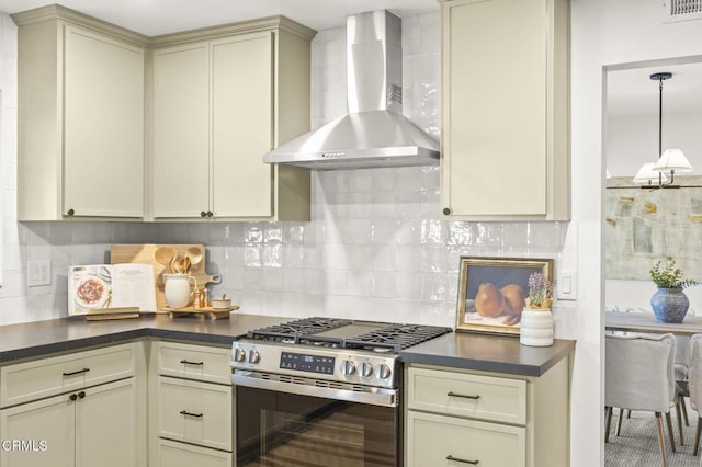 kitchen with cream cabinetry, gas range, wall chimney exhaust hood, decorative light fixtures, and backsplash