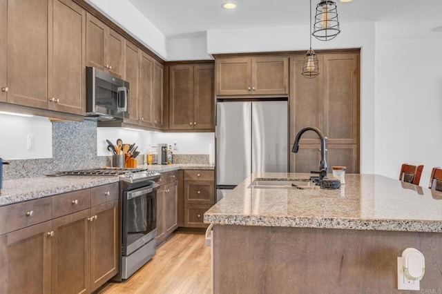 kitchen featuring appliances with stainless steel finishes, an island with sink, sink, light hardwood / wood-style flooring, and decorative light fixtures