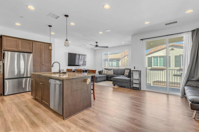 kitchen with sink, decorative light fixtures, light stone counters, an island with sink, and appliances with stainless steel finishes