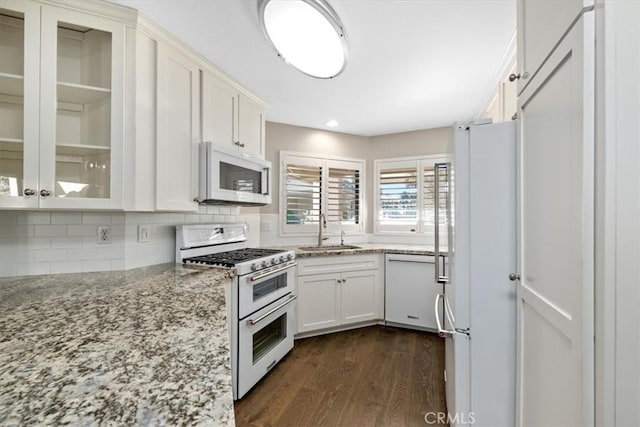 kitchen with white appliances, light stone countertops, backsplash, white cabinetry, and sink