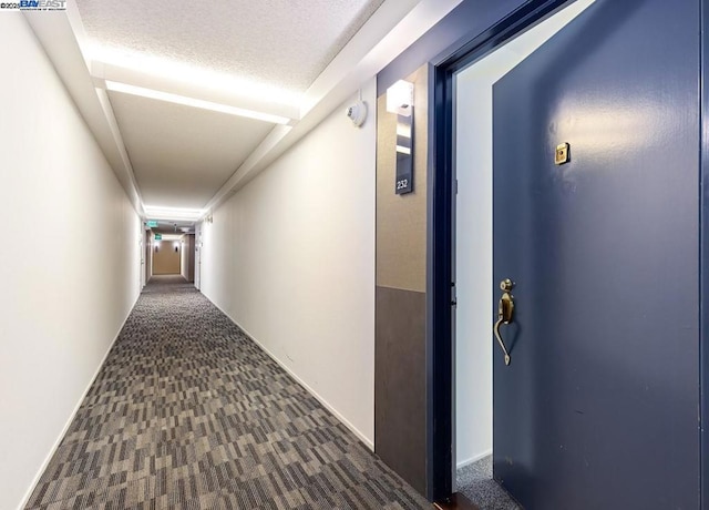 hallway with a textured ceiling and dark colored carpet