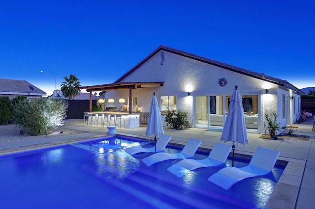 pool at dusk with a patio and exterior bar