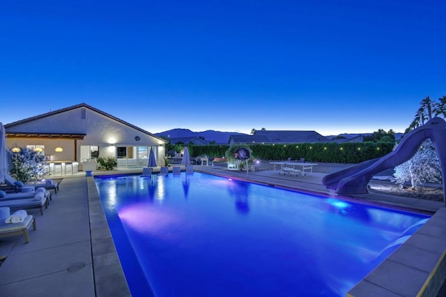 pool at dusk featuring a patio area and a water slide