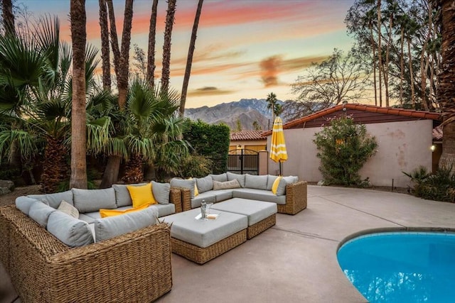 pool at dusk featuring a mountain view, an outdoor hangout area, and a patio