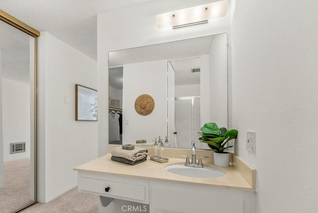 bathroom featuring a textured ceiling, walk in shower, and vanity