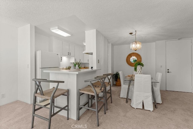 kitchen featuring decorative light fixtures, white cabinetry, white refrigerator, light carpet, and kitchen peninsula