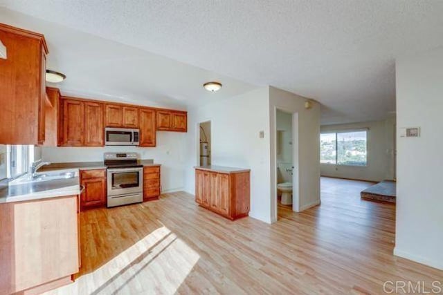 kitchen featuring sink, a textured ceiling, light wood-type flooring, and appliances with stainless steel finishes