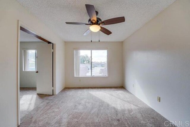 carpeted empty room with a textured ceiling, ceiling fan, and a wealth of natural light