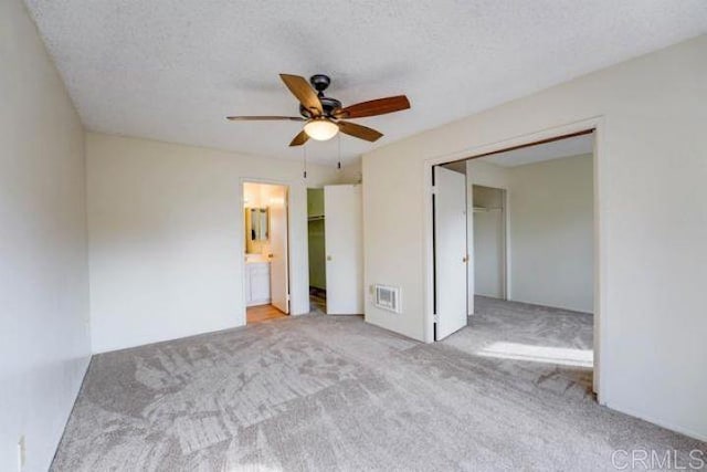 unfurnished bedroom featuring ensuite bath, a textured ceiling, a closet, ceiling fan, and light carpet