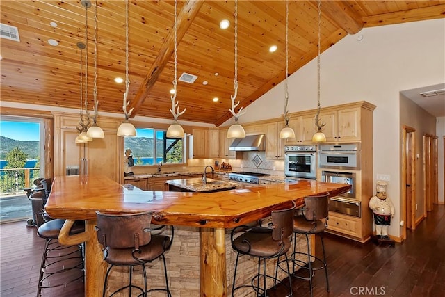 kitchen with decorative light fixtures, backsplash, exhaust hood, a center island with sink, and sink