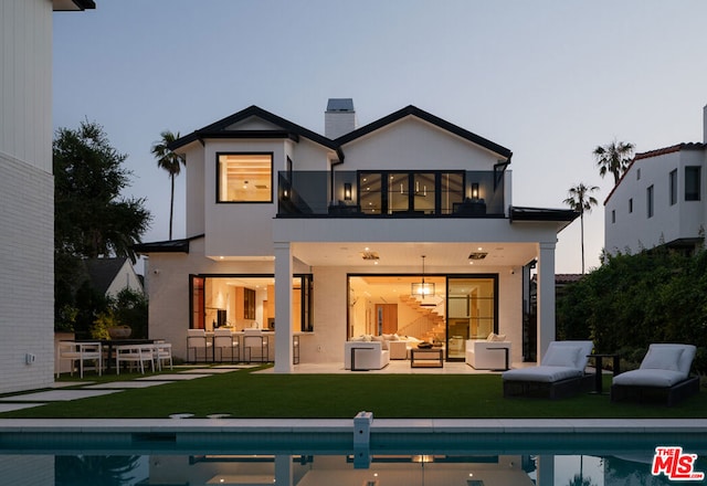 back house at dusk featuring a balcony, a patio area, a lawn, and an outdoor living space