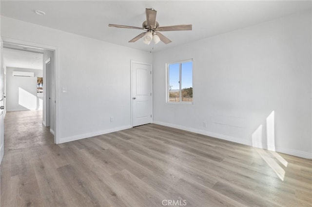 spare room with light wood-type flooring, ceiling fan, and an AC wall unit