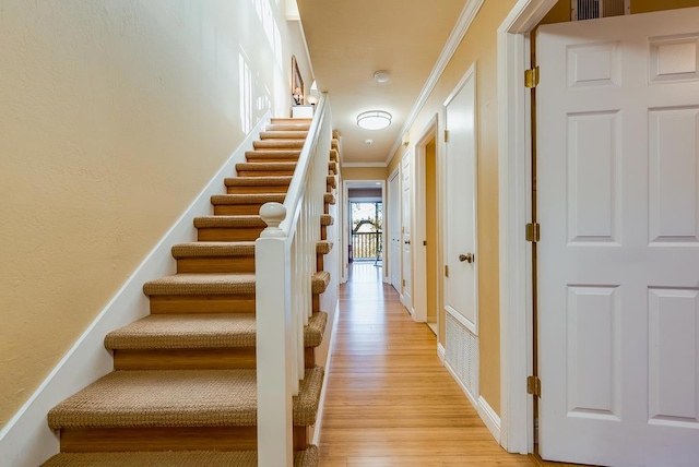 stairs with crown molding and wood-type flooring