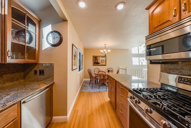 kitchen with decorative light fixtures, stainless steel appliances, dark stone counters, light hardwood / wood-style floors, and a chandelier