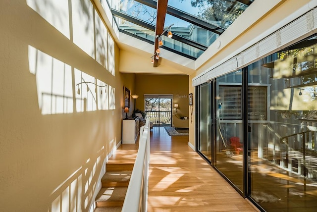 hallway with a high ceiling, a skylight, and light wood-type flooring