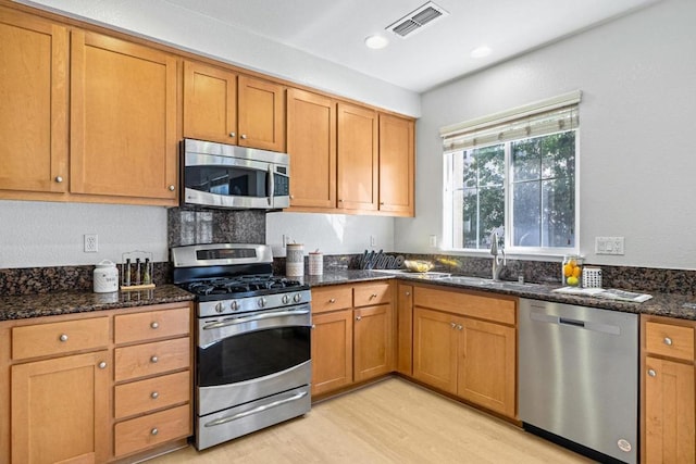 kitchen featuring light wood-type flooring, appliances with stainless steel finishes, dark stone countertops, and sink