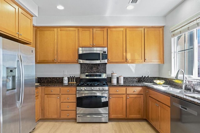 kitchen featuring light hardwood / wood-style floors, sink, stainless steel appliances, and dark stone counters