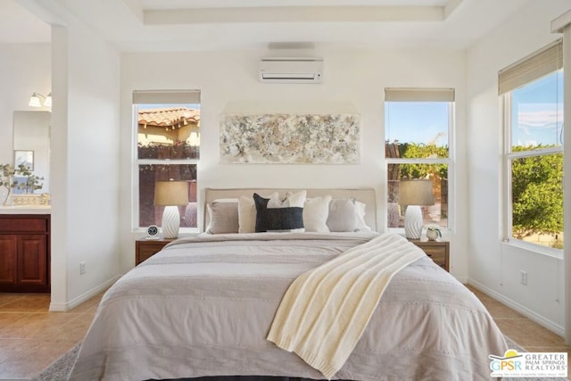 bedroom featuring a wall mounted AC, a tray ceiling, light tile patterned floors, and connected bathroom