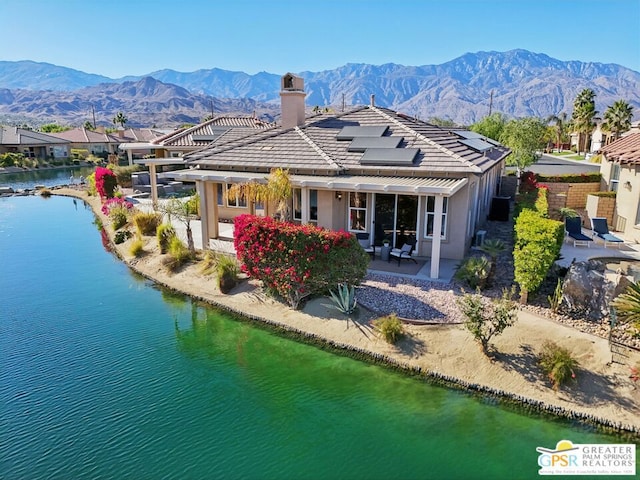 rear view of house featuring solar panels, a water and mountain view, and a patio