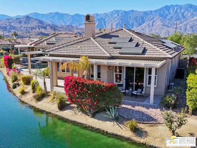 rear view of house with solar panels, a water and mountain view, and a patio