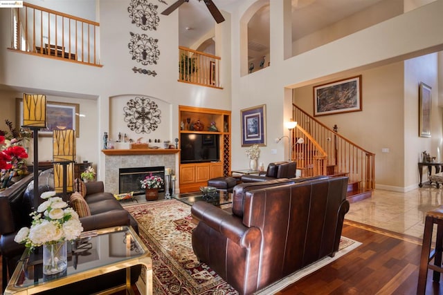 living room with a high ceiling, a fireplace, ceiling fan, and dark wood-type flooring