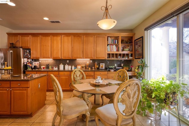 kitchen featuring light tile patterned floors, dark stone counters, pendant lighting, high end refrigerator, and tasteful backsplash