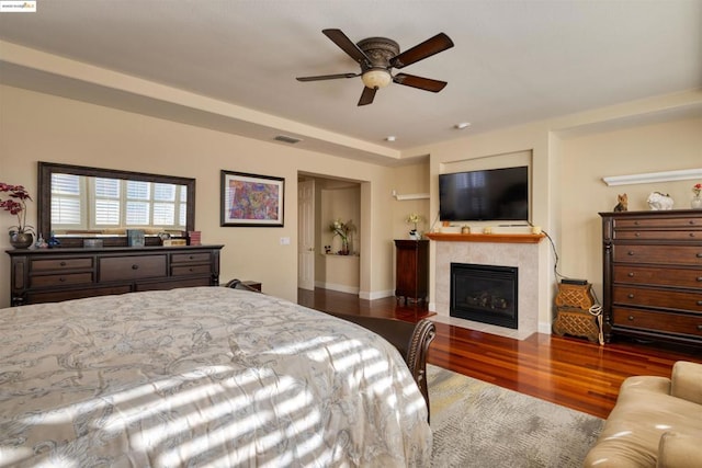 bedroom featuring a tiled fireplace, ceiling fan, and hardwood / wood-style floors