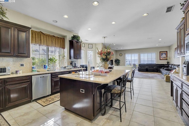 kitchen with a kitchen bar, dishwasher, a kitchen island with sink, and light tile patterned flooring