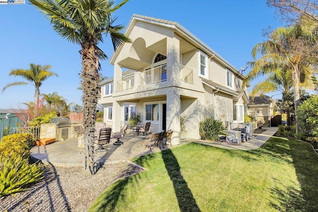 back of house with a balcony, a patio area, an outdoor kitchen, and a yard