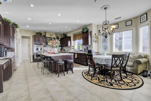 kitchen featuring dark brown cabinetry, a kitchen island, hanging light fixtures, a chandelier, and light tile patterned floors