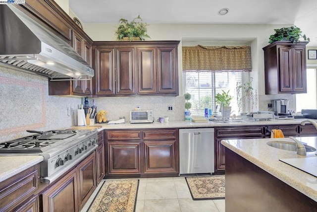 kitchen with appliances with stainless steel finishes, light tile patterned floors, wall chimney range hood, sink, and backsplash