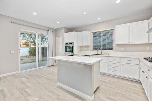 kitchen with stainless steel appliances, light wood-type flooring, a kitchen island, sink, and white cabinetry