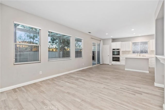 unfurnished living room with light hardwood / wood-style floors, sink, and plenty of natural light