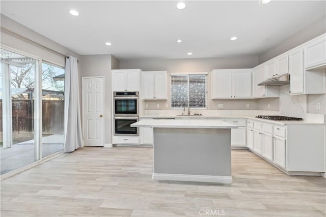 kitchen with appliances with stainless steel finishes, white cabinetry, sink, and a kitchen island