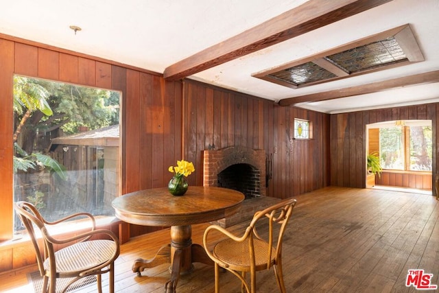 dining area featuring beamed ceiling, wooden walls, hardwood / wood-style floors, and a brick fireplace