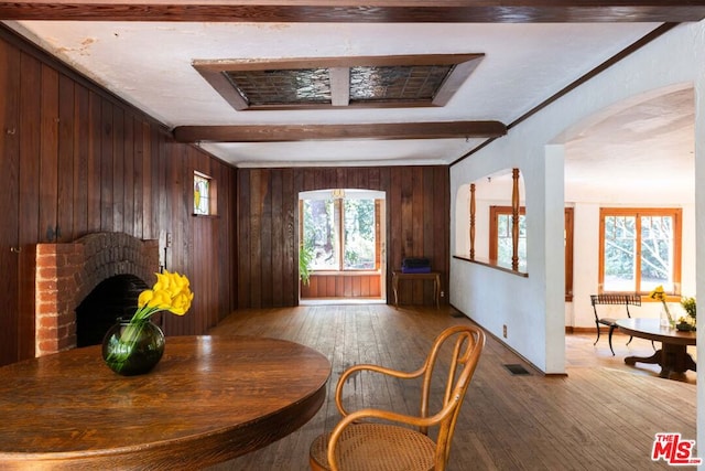 dining room featuring hardwood / wood-style flooring, beamed ceiling, and wood walls