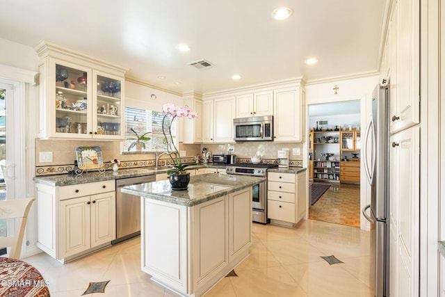 kitchen with a kitchen island, dark stone counters, light tile patterned floors, and appliances with stainless steel finishes