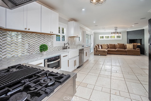 kitchen with white cabinetry, stainless steel appliances, a fireplace, backsplash, and crown molding