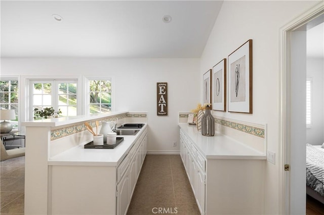 kitchen with sink, white cabinetry, lofted ceiling, kitchen peninsula, and tile patterned floors