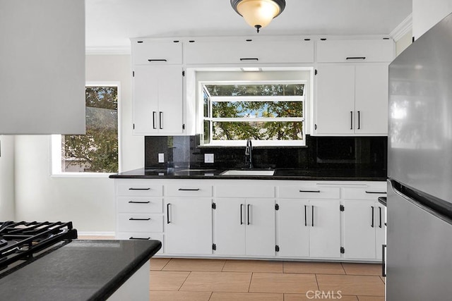 kitchen featuring sink, white cabinetry, crown molding, and stainless steel refrigerator