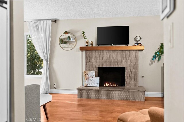 living room with a textured ceiling, hardwood / wood-style floors, and a tiled fireplace