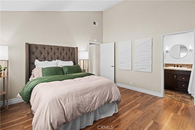 bedroom featuring lofted ceiling, dark hardwood / wood-style flooring, ensuite bathroom, and sink