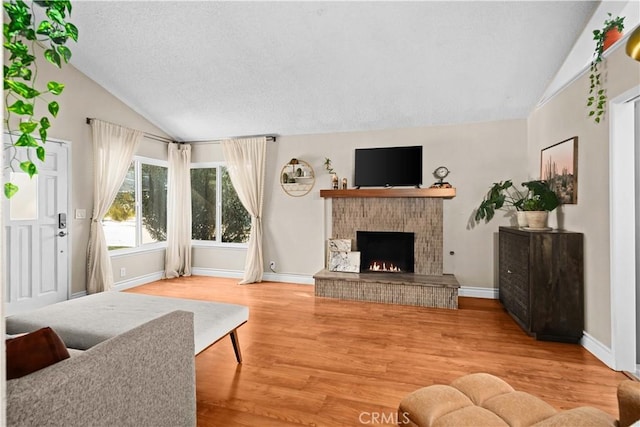 living room with wood-type flooring, vaulted ceiling, a brick fireplace, and a textured ceiling