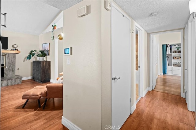 hallway with lofted ceiling, a textured ceiling, and light wood-type flooring